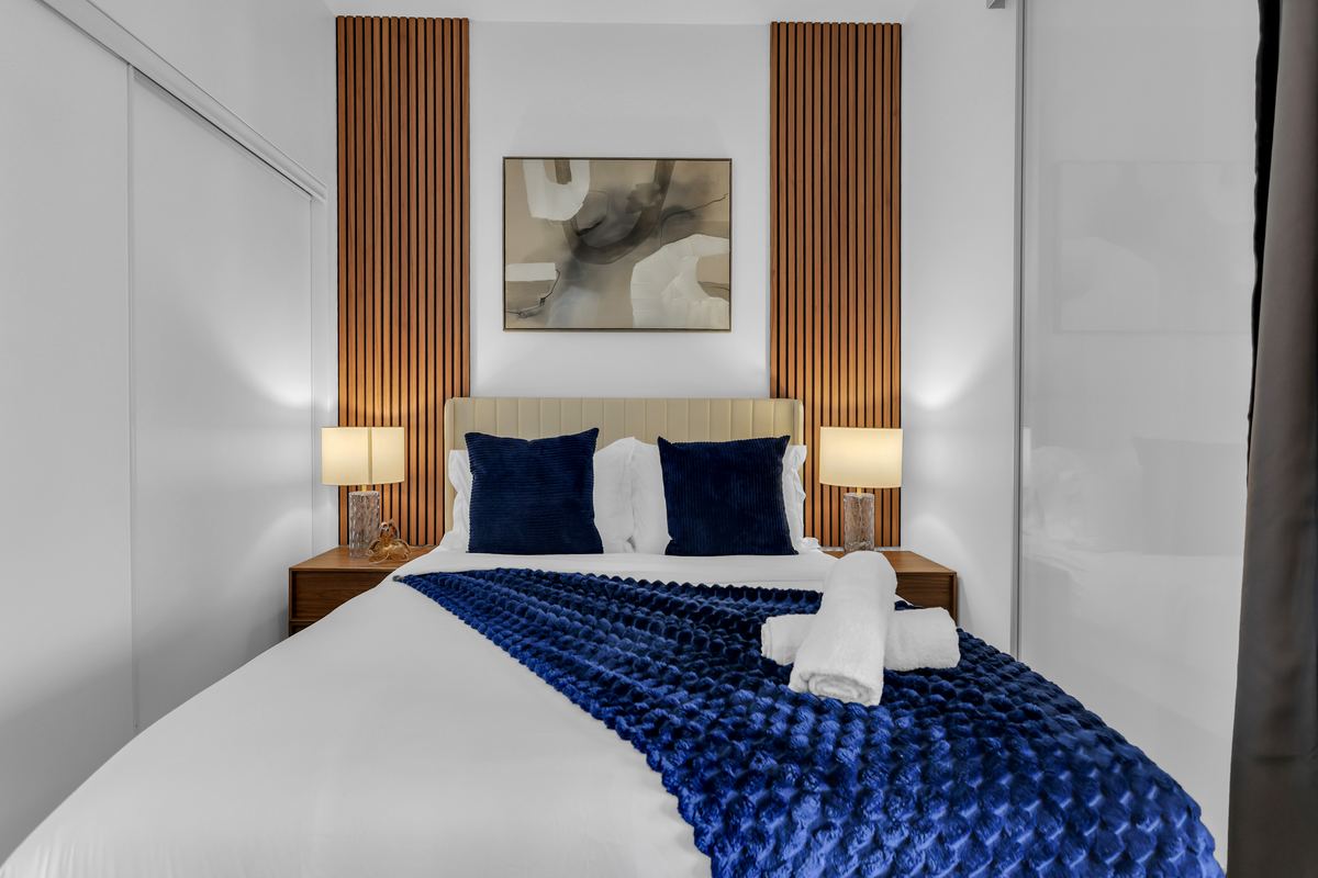 Bedroom with slatted wood panels, navy bedding and bedside lamps