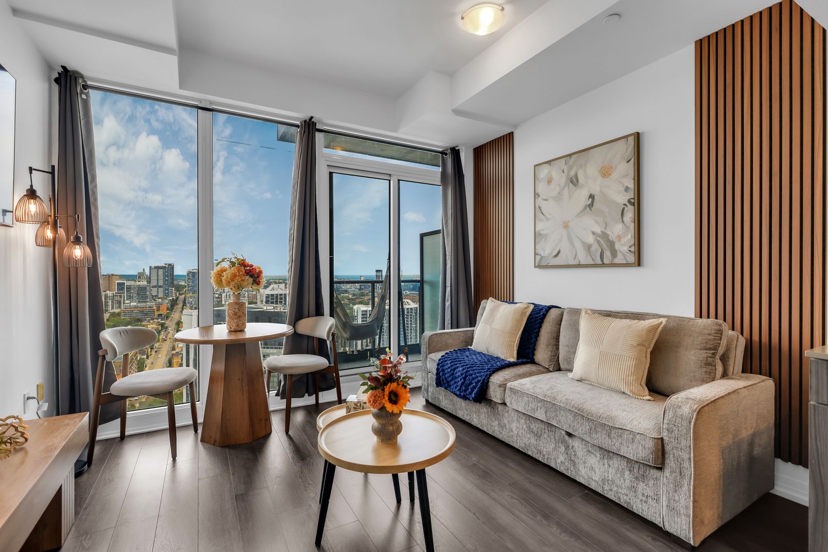 Dining table and living room beside floor-to-ceiling windows looking over downtown Toronto