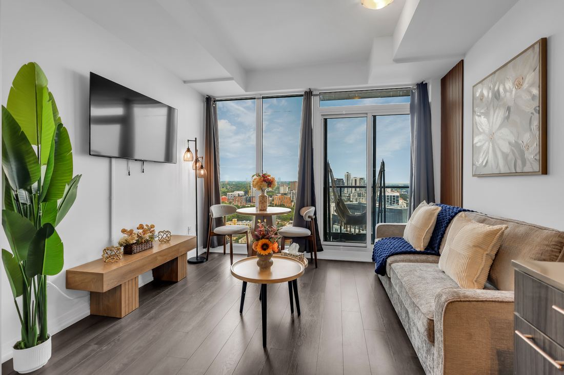Living room with a wall-mounted TV, dining table and floor-to-ceiling windows over the city